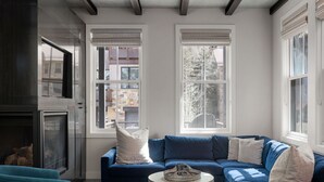 Una sala de estar moderna con un sofá seccional azul, una chimenea y ventanas amplias con persianas.