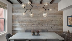Un comedor con pared de madera, una lámpara moderna y una mesa con sillas.