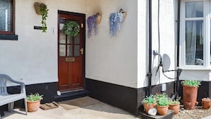 Una entrada de casa con puerta de madera, un adorno de bienvenida y plantas en macetas.