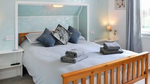 Un dormitorio con cama, almohadas, mesita de noche, lámpara y ventana con cortinas.