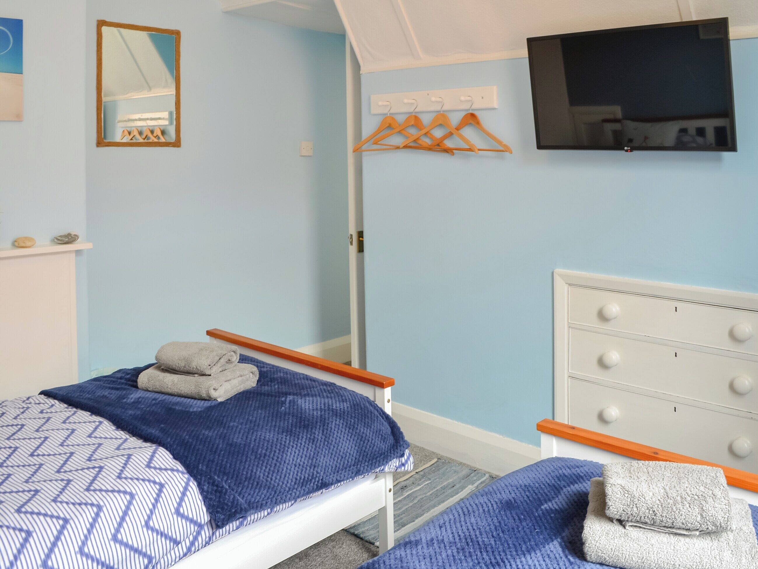 A bedroom with two beds, a TV mounted on the wall, a wooden bench, a mirror, and a clothing rack.