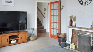 Una sala de estar con televisor, chimenea, escalera y una puerta con paneles de vidrio esmerilado.