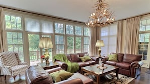 A spacious living room with leather sofas, a patterned armchair, and a chandelier. - Bearities - 2 homes, sleeps 28, hot tubs, grills! (Killington)