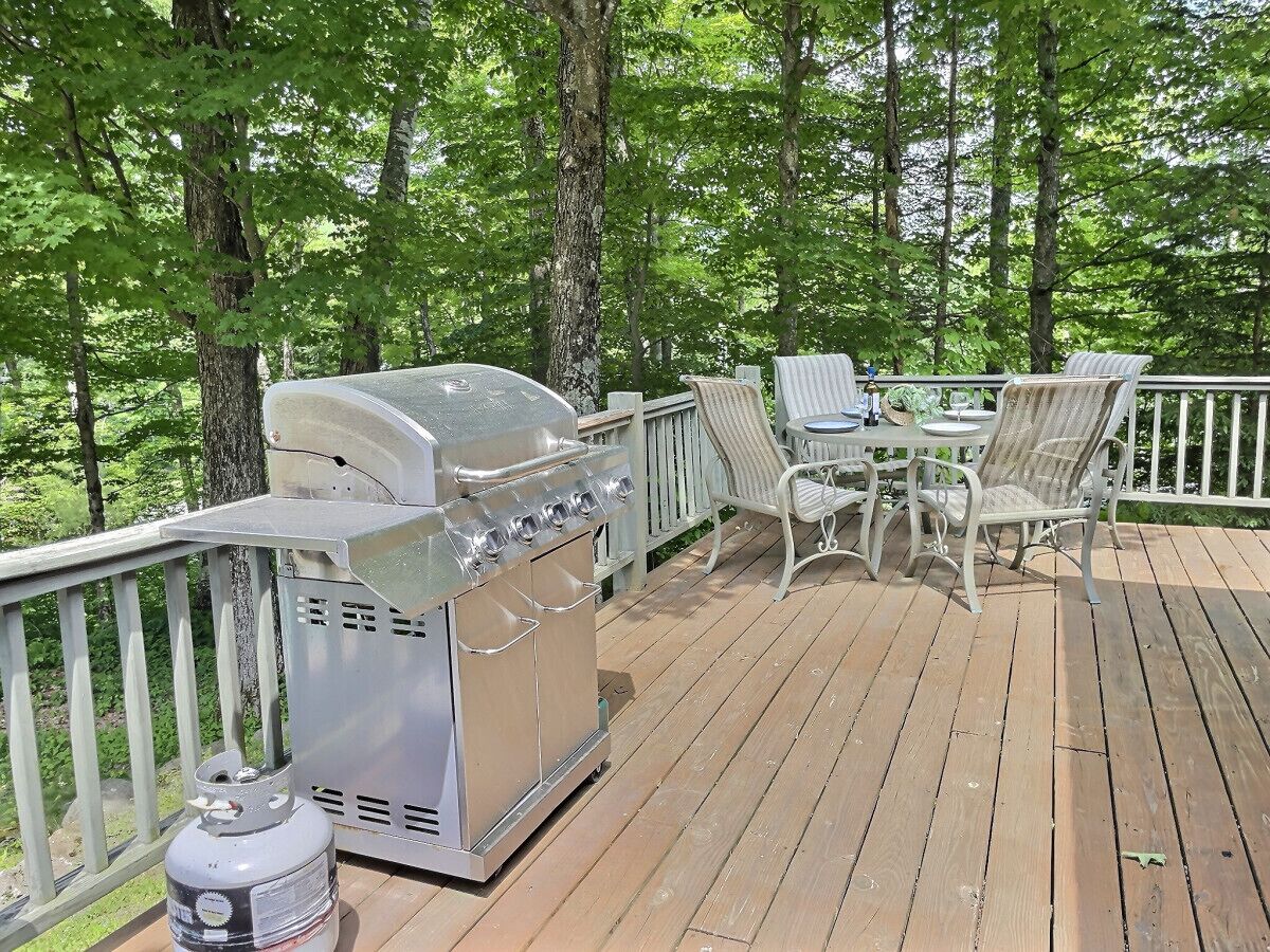 A deck with a barbecue grill, outdoor seating, and a propane tank.