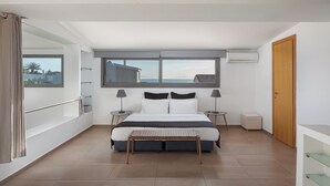 Ein Schlafzimmer mit einem großen Bett, zwei Nachttischen, einem Fenster mit Ausblick, einer Holztür und einem Balkon mit Geländer.