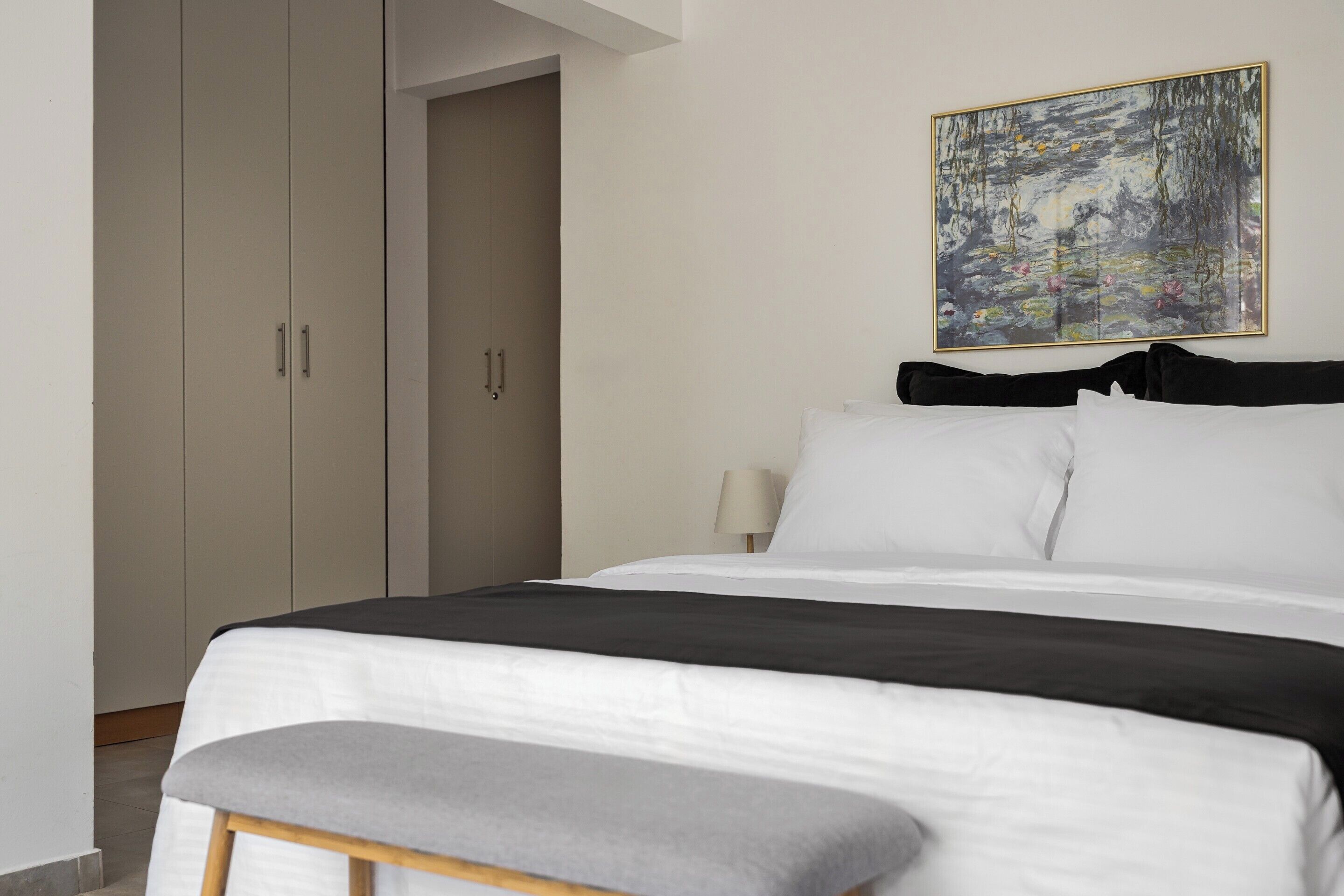 A bedroom with a bed, a bench, a wardrobe, and a painting on the wall.