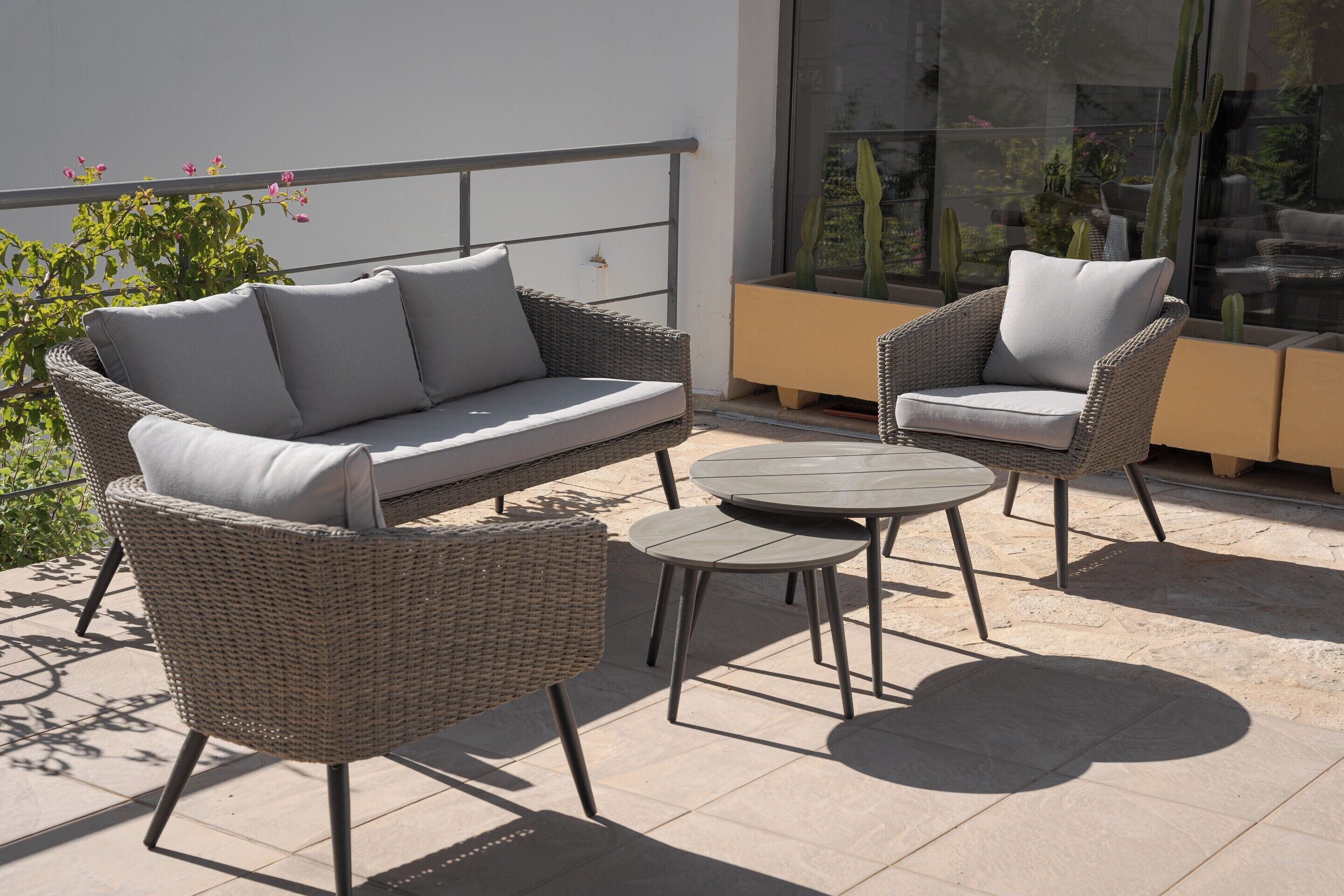 Een terras met rieten meubels en een glazen omheining.