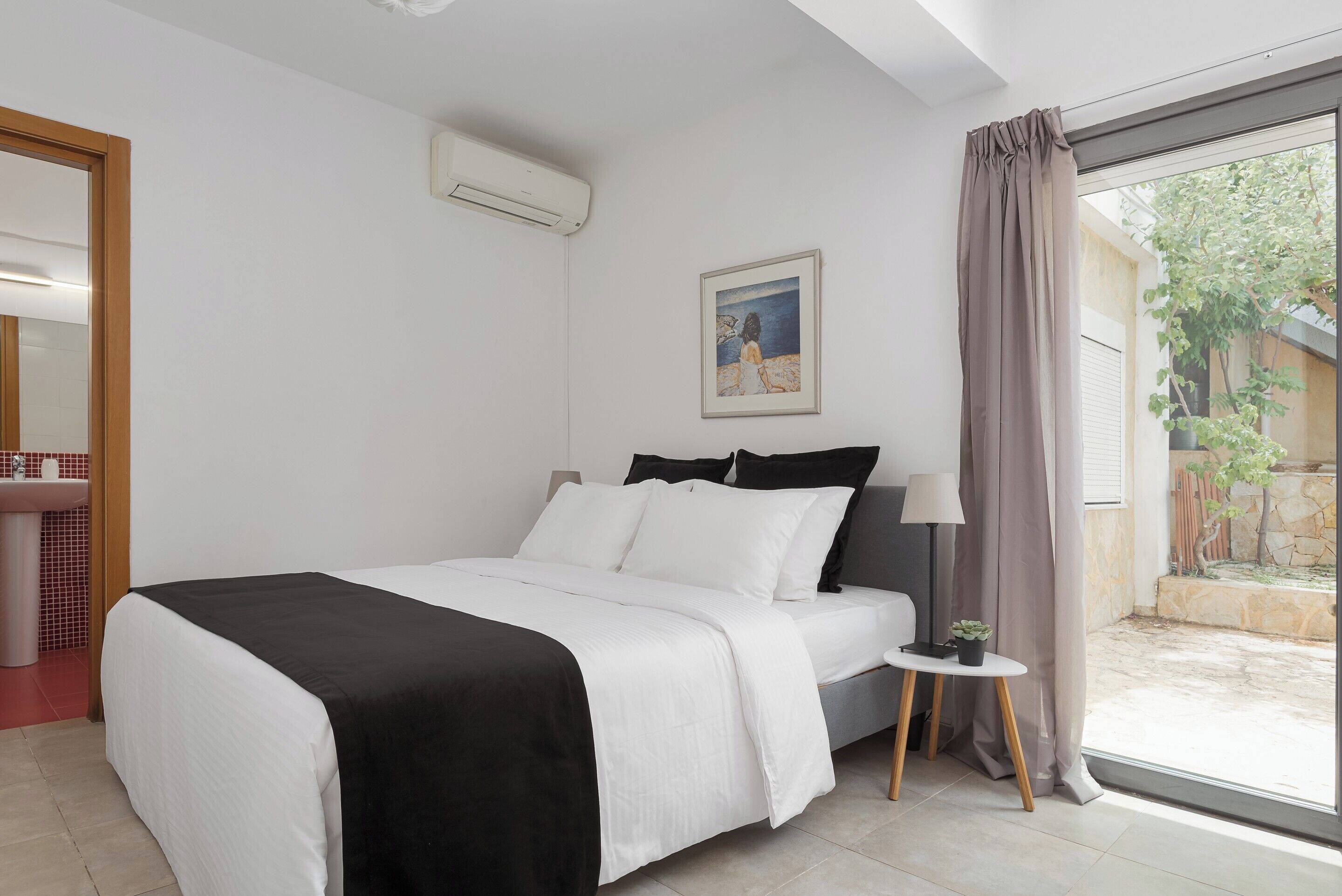 Un dormitorio con cama, mesita de noche, lámpara y ventana con cortinas.