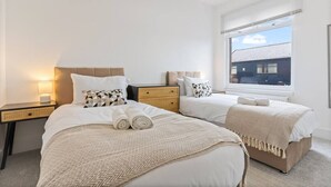 Une chambre d’hôtel avec deux lits, une table de chevet, une lampe et une fenêtre avec des stores.