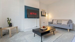 Un salon moderne avec un canapé gris, une table basse noire et un téléviseur fixé au mur qui affiche le logo « NETFLIX ».