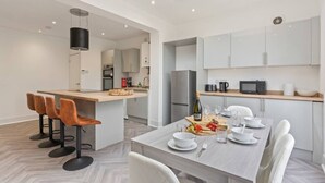 Une cuisine moderne avec des meubles blancs, un îlot central et un coin repas avec des chaises blanches.
