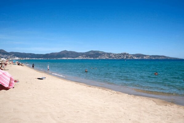 Une plage avec un rivage sablonneux, une eau d’un bleu limpide et des montagnes qui se dessinent à l’horizon.