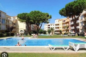 Une piscine entourée d’immeubles d’appartements dotés de balcons, d’arbres et de chaises longues.