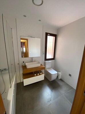 Bathroom features a sink, mirror, and toilet, with a window and grey tile flooring.
