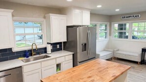 A kitchen with white cabinets, a stainless steel refrigerator, a wooden countertop, and a sign that reads 'OUR HAPPY PLACE'. - Cozy lake retreat in Sand Point! Game room with deck and views of Lake Texoma. (Mead)