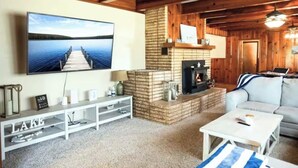 A cozy living room with a fireplace, a television mounted on the wall, a sofa, and a coffee table. - Cozy lake retreat in Sand Point! Game room with deck and views of Lake Texoma. (Mead)