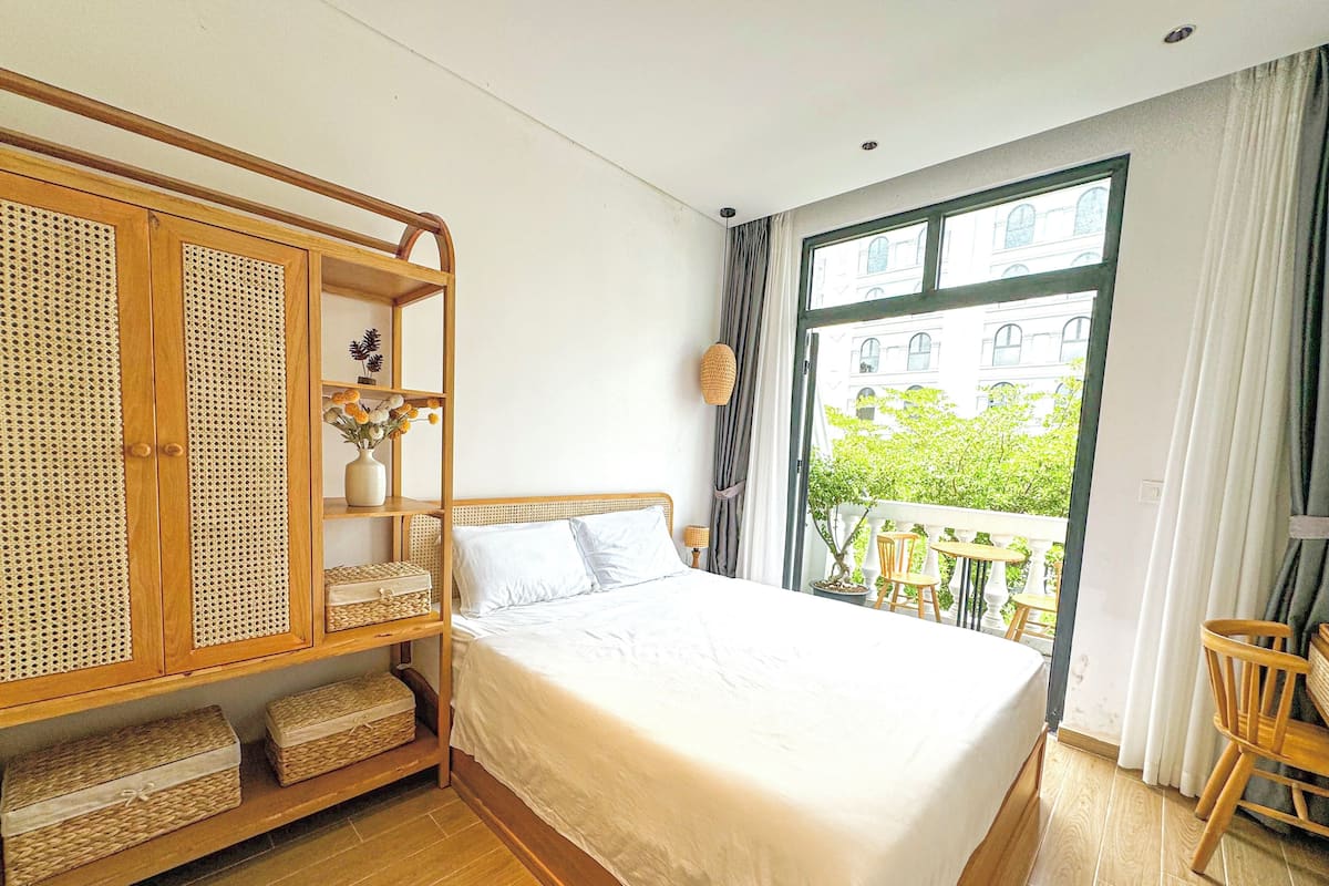 Un dormitorio con una cama grande, armario de madera, cestas de mimbre y un balcón con mobiliario exterior.