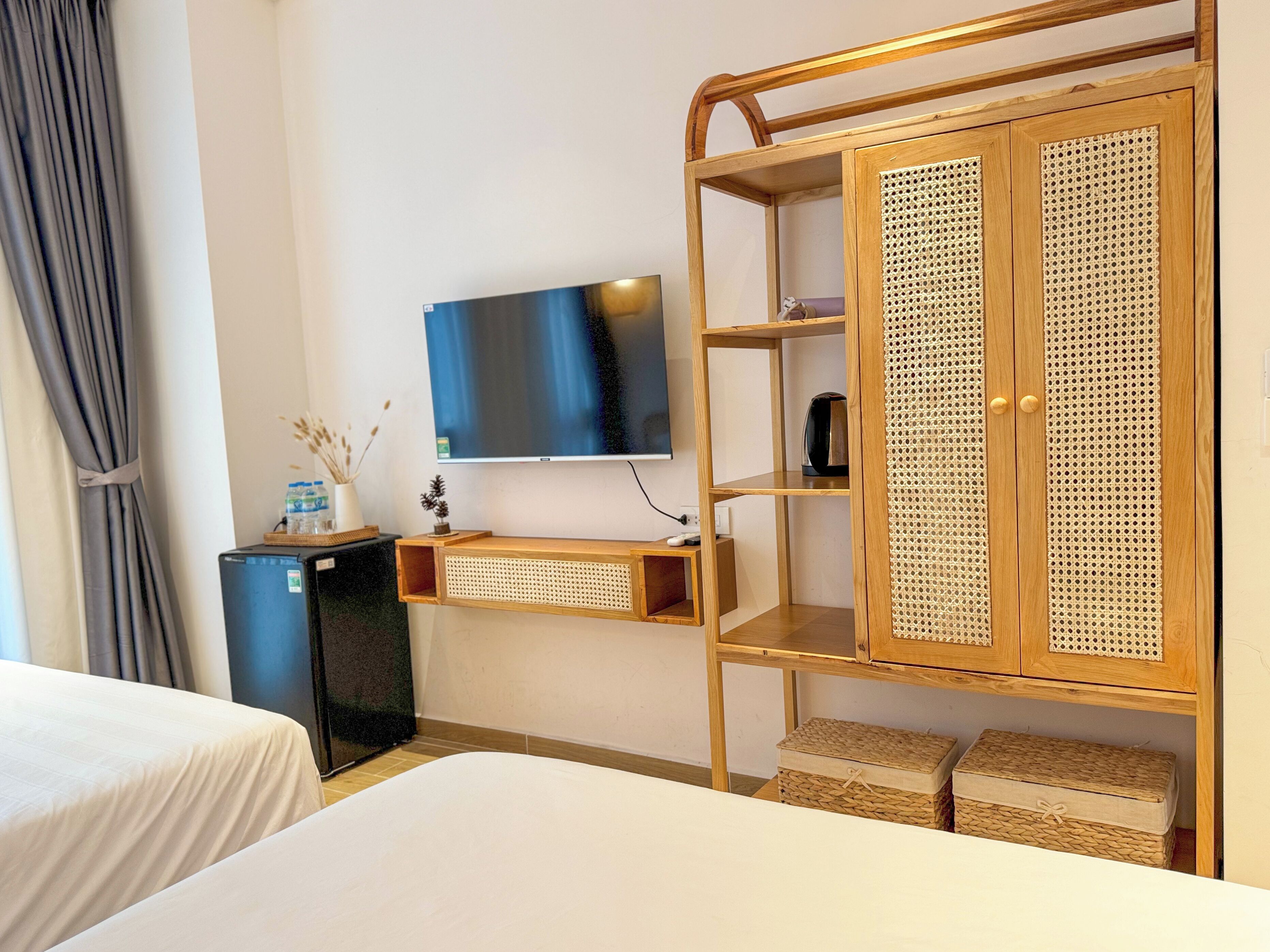 A hotel room with a bed, a TV, a wardrobe, and a small desk with a lamp and a water bottle.