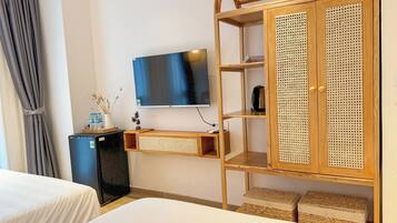 A hotel room with a bed, a TV, a wardrobe, and a small desk with a lamp and a water bottle.