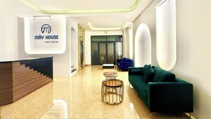 Un moderno hall de hotel con mostrador de recepción, una escalera, un sofá verde y un cartel que dice 'MAY HOUSE mini hotel'.