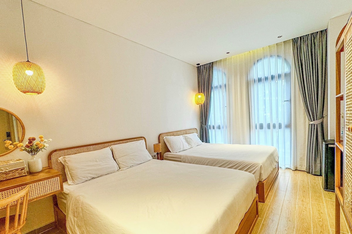 Habitación de hotel con dos camas, un escritorio de madera, un espejo y una lámpara colgante.