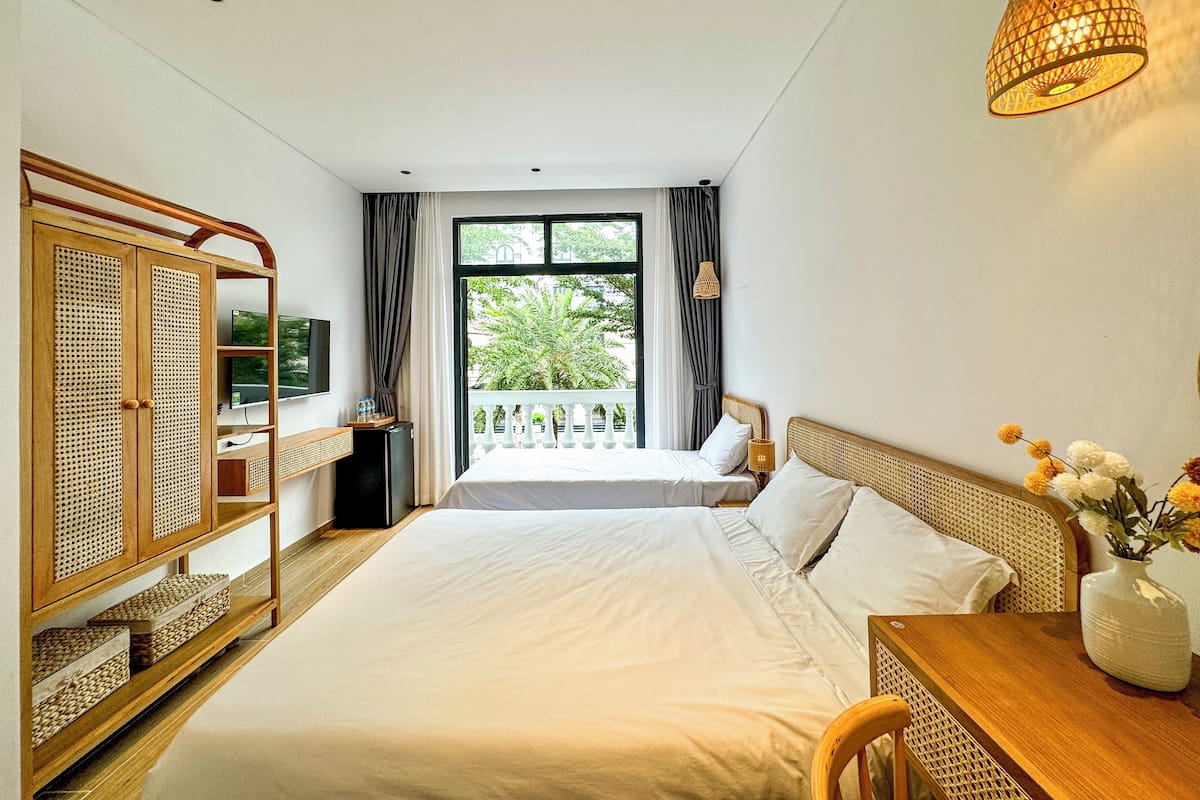 Habitación de hotel con dos camas, televisión, escritorio, silla, armario y balcón con vistas a zonas verdes.