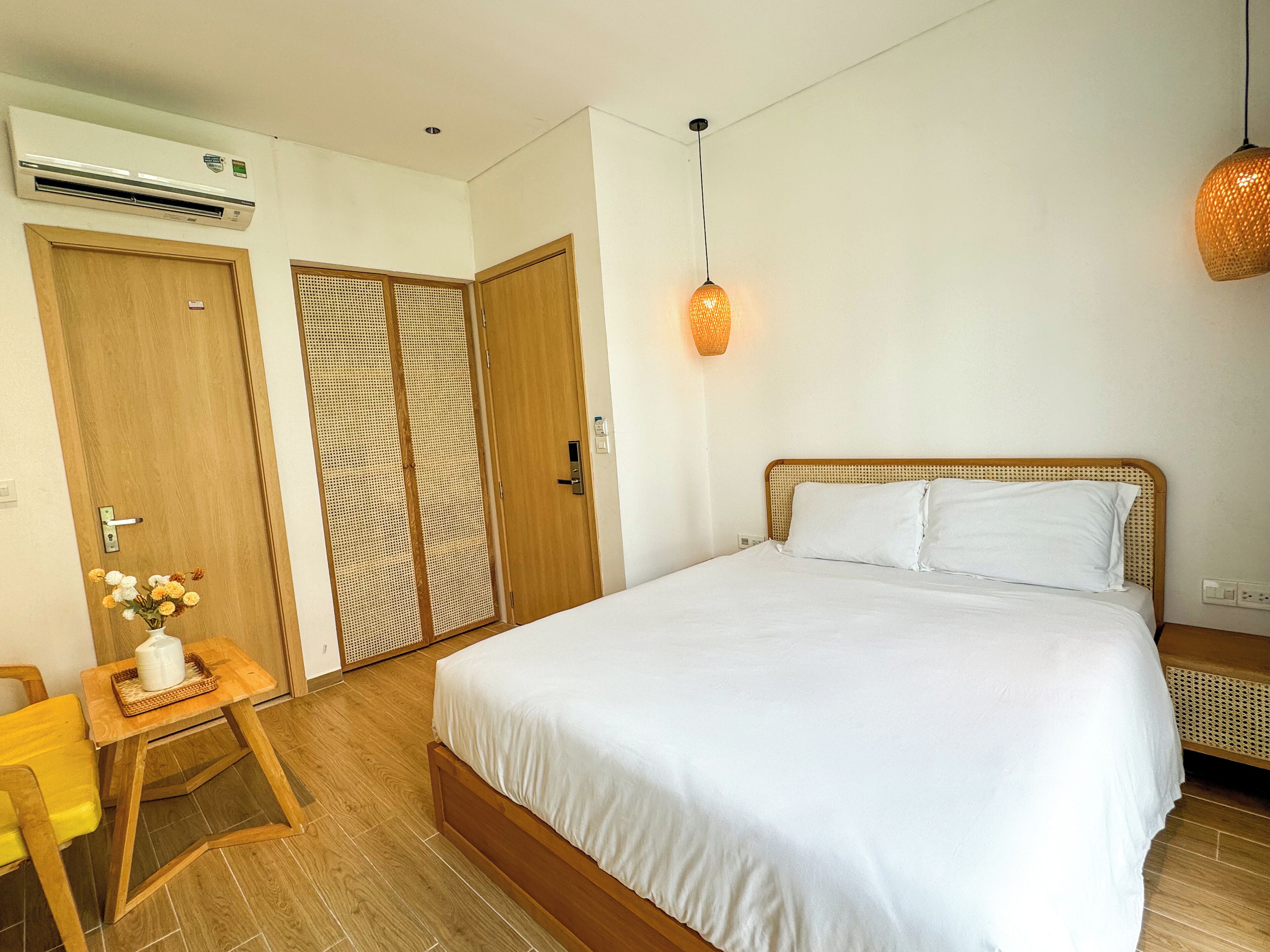 Una camera da letto con un letto, un comodino con un vaso di fiori, una sedia di legno e un armadio con una porta in rattan.