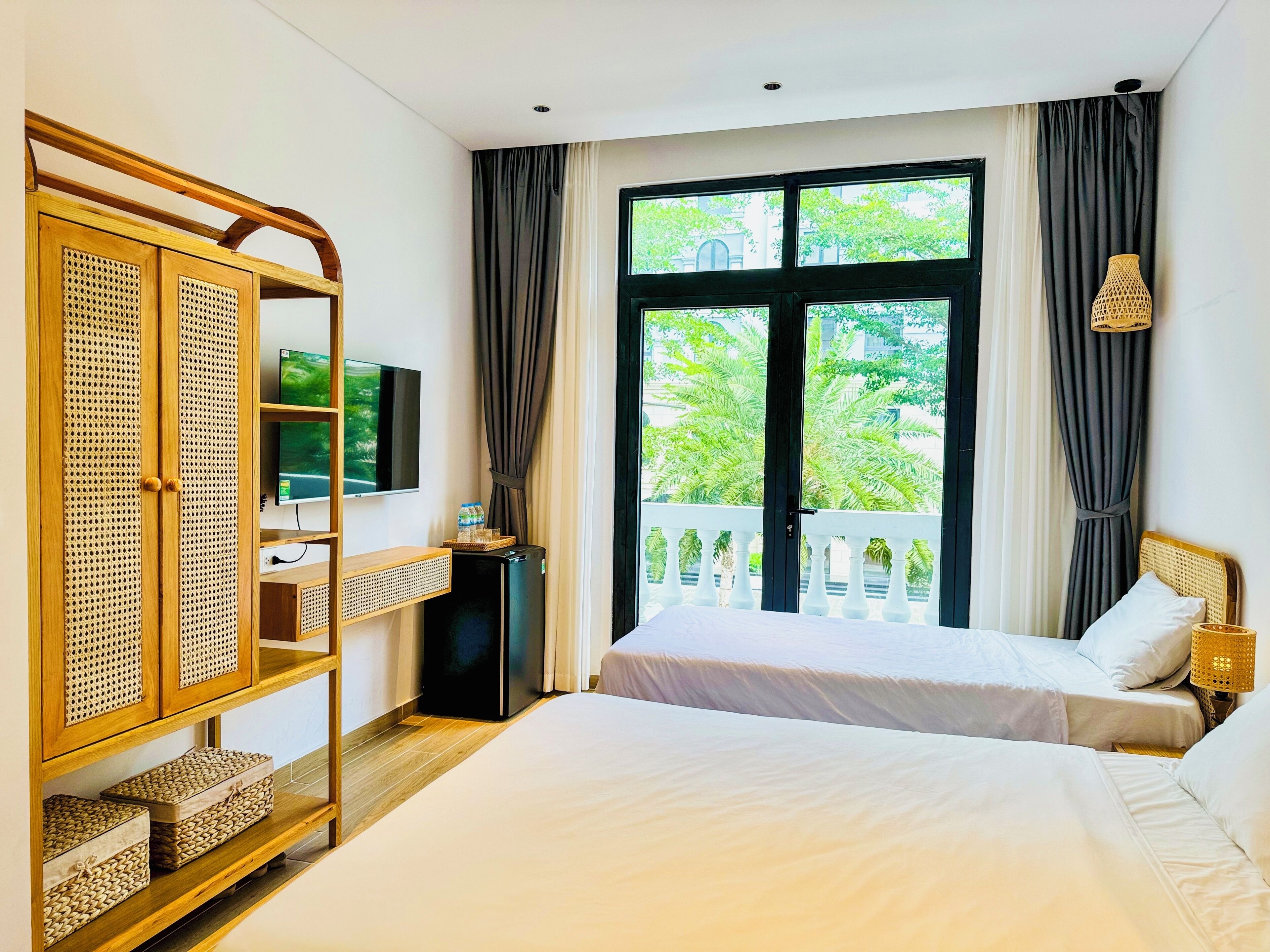 A bedroom with two beds, a TV, a wardrobe, and a balcony with curtains.