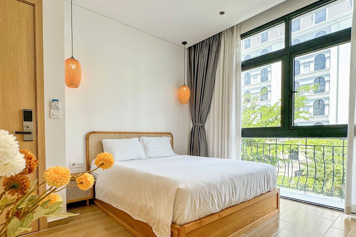 Un dormitorio con cama de madera, ropa de cama blanca, vistas a un balcón y una ventana con cortinas.