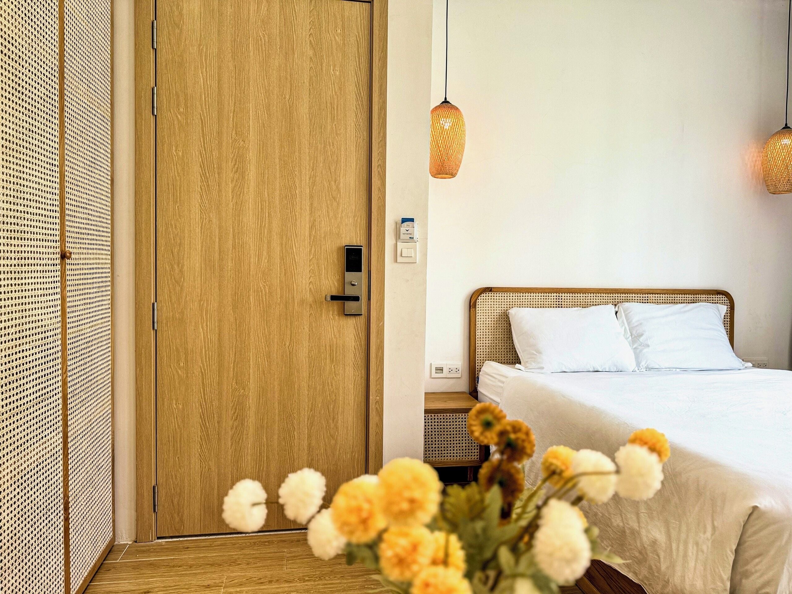Quarto com porta de madeira, cama com lençóis brancos, duas luminárias pendentes e uma pequena mesa de cabeceira.