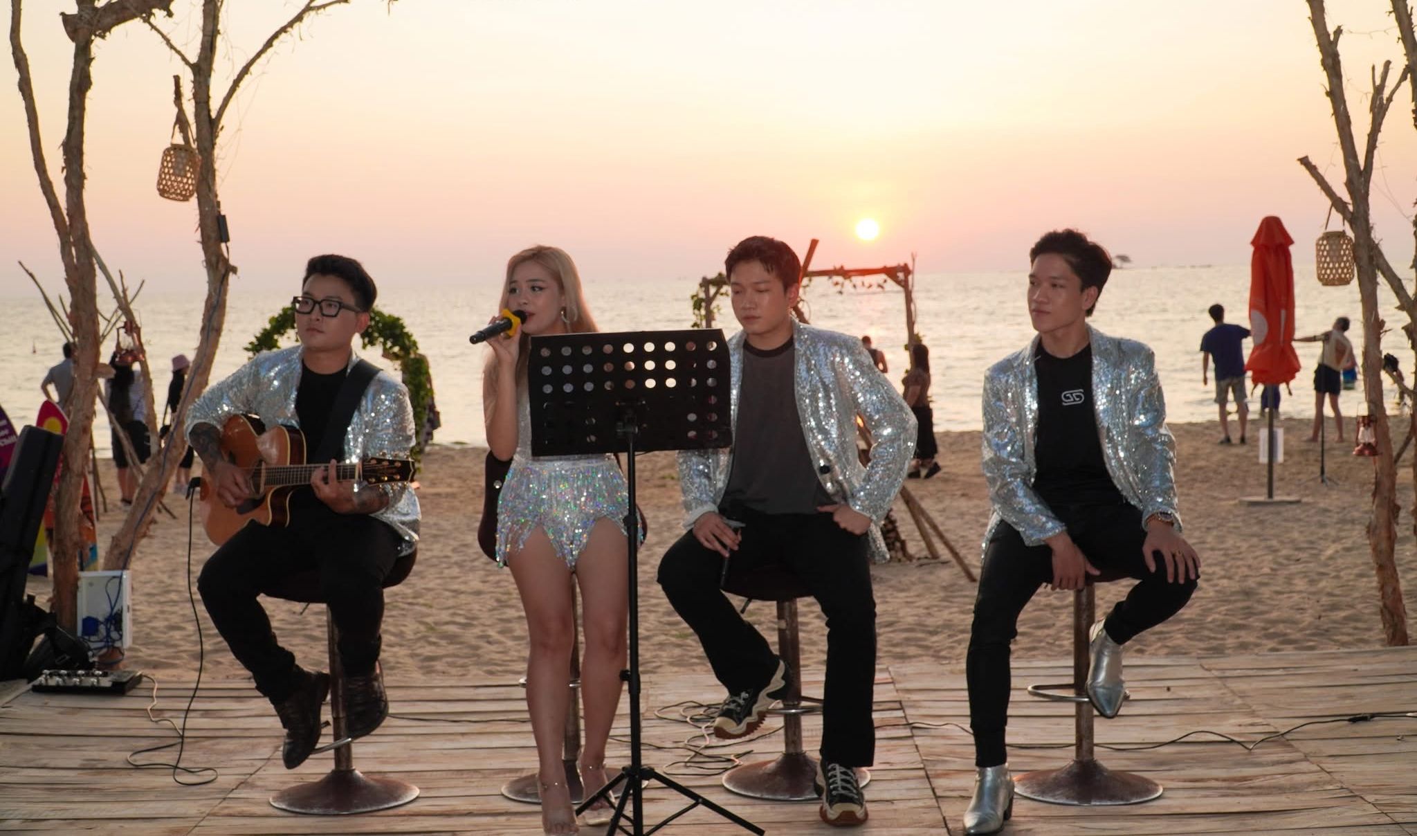 Esibizione sulla spiaggia con musicisti e un cantante, con il tramonto sullo sfondo.