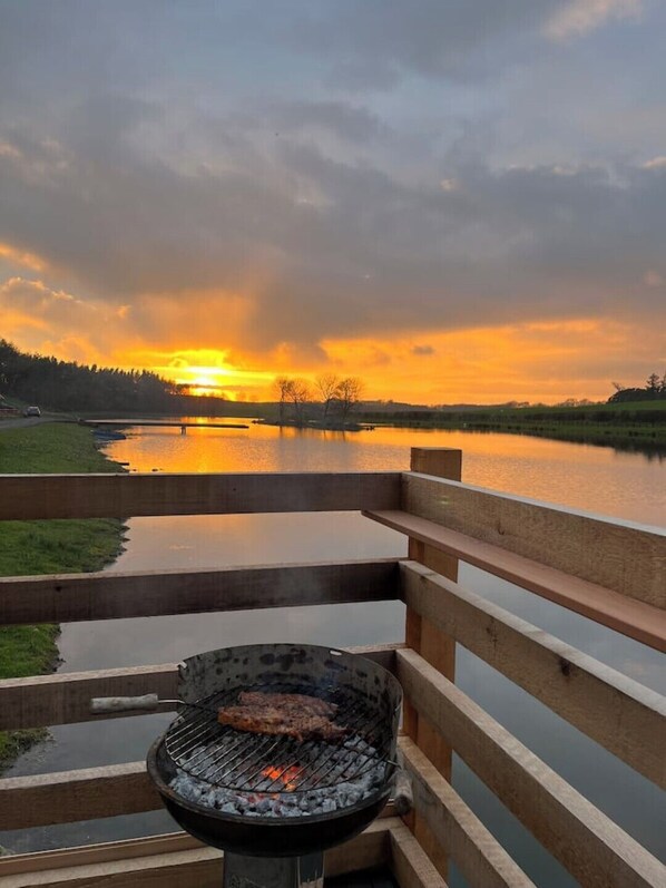 Grill med udsigt til solnedgang over et sø.