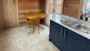 Cocina compacta con techo de madera, una mesa redonda de madera y un lavamanos integrado.