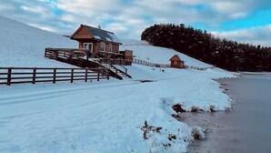 A snow-covered landscape with a wooden cabin and a small building on a hill. - Cedar Lodge - Idyllically situated Lakeside & private hot tub fishing riding (Northumberland)