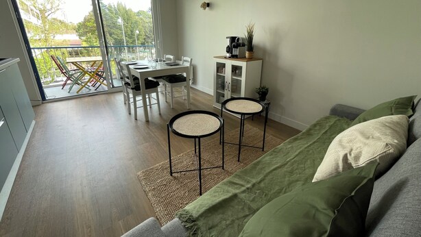 A modern living room with a green sofa, a dining area with a white table and chairs, and a balcony with a view of trees and buildings. - Proche Gare, Commerce et Plage Avenue Louis Lajarrige (La Baule-Escoublac)