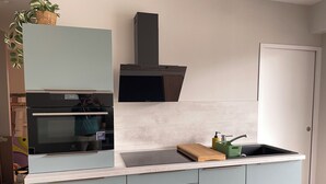 A modern kitchen with a built-in oven, a stainless steel range hood, and a sink with a wooden cutting board and green utensil holder. - Proche Gare, Commerce et Plage Avenue Louis Lajarrige (La Baule-Escoublac)