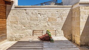 Un banco de madera y una cesta de mimbre con follaje frente a una pared de piedra.