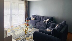 A modern living room with a dark blue sofa, a glass coffee table, and a decorative vase. - Luxurious 2 Bedroom Apartment - Alma by Cytonn (Ruaka)