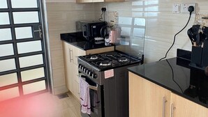 A kitchen with a gas stove, microwave, and a coffee maker. There are wooden cabinets and a tiled backsplash. - Luxurious 2 Bedroom Apartment - Alma by Cytonn (Ruaka)