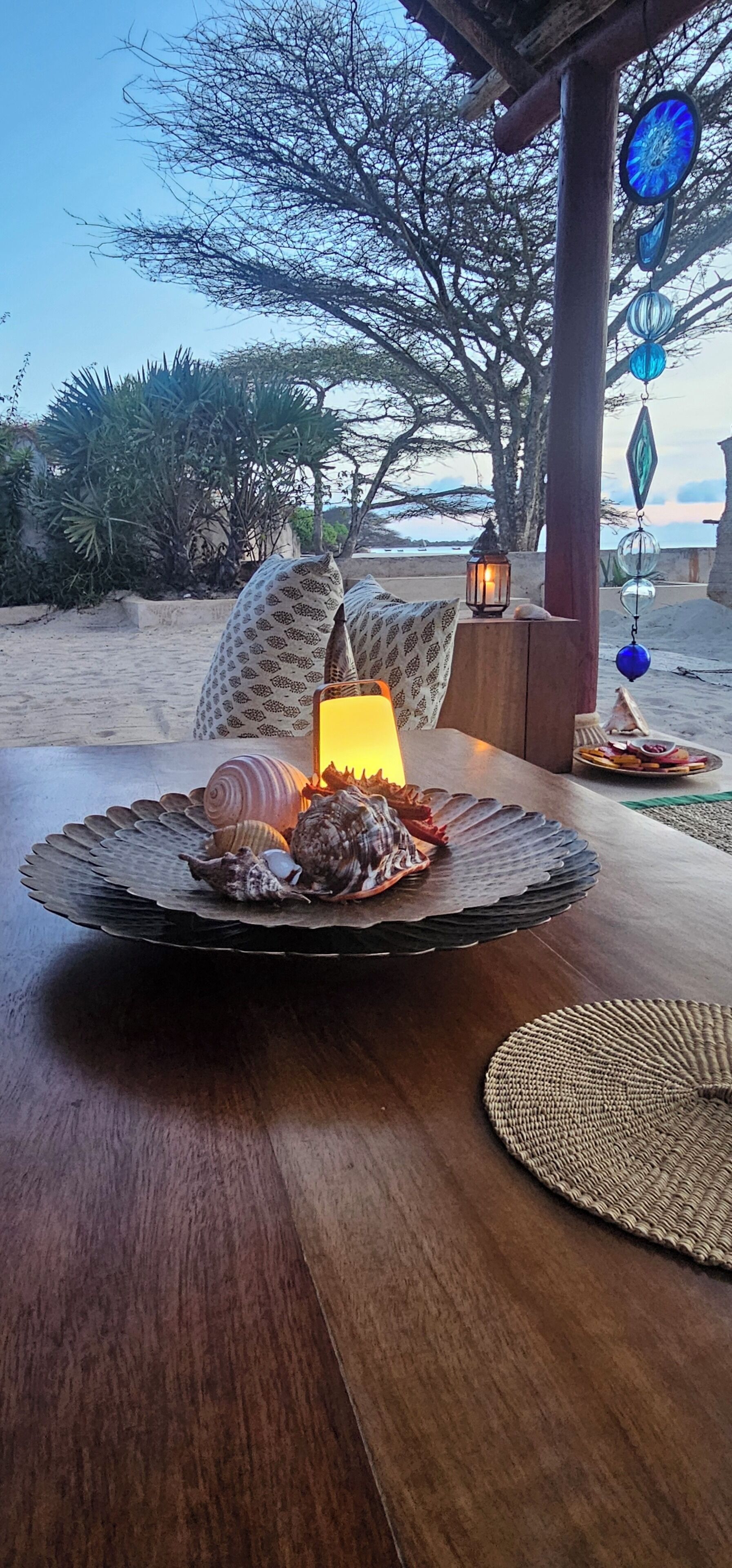 A wooden table with a decorative plate of seashells and a lantern.