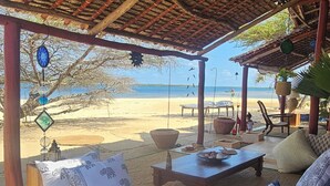 A beachside lounge with a thatched roof, outdoor seating, and a view of the beach and ocean.