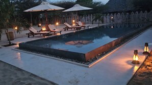Ein Swimmingpool mit Liegestühlen und Sonnenschirmen, umgeben von einer Steinmauer und Palmen.