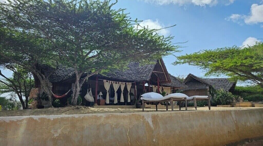 Une maison traditionnelle à toit de chaume, dotée d’une véranda et entourée d’arbres.