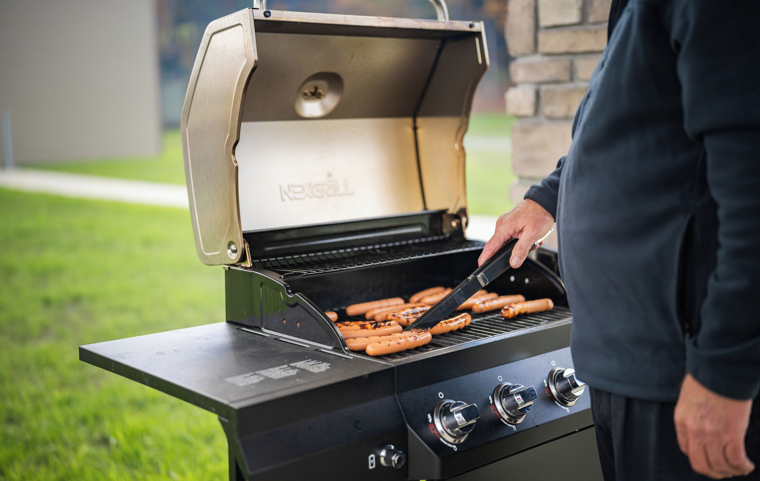 A person grilling hot dogs on an outdoor grill.