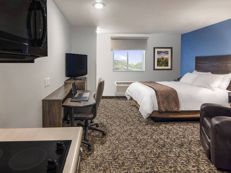 A hotel room with a bed, desk, chair, TV, and a view of the outdoors.