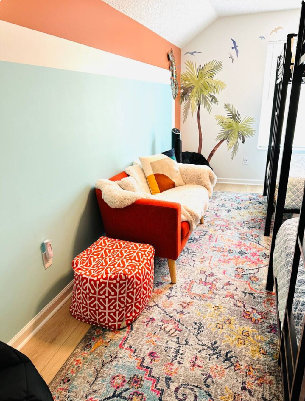 Een gezellige kamer met een rode bank, een gestreept voetenbankje, een decoratieve wand en een kleurrijk vloerkleed.