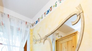 Ein Zimmer mit einem großen Spiegel, einem fensterförmigen Öffnung mit Vorhang und einer Holztür.