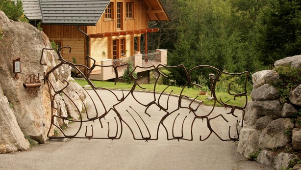 Eine Holzhütte mit geneigtem Dach, einem Steintor und bewaldeter Umgebung.