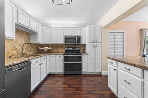A kitchen with white cabinets, a granite countertop, a built-in microwave, a double oven, and a dishwasher.