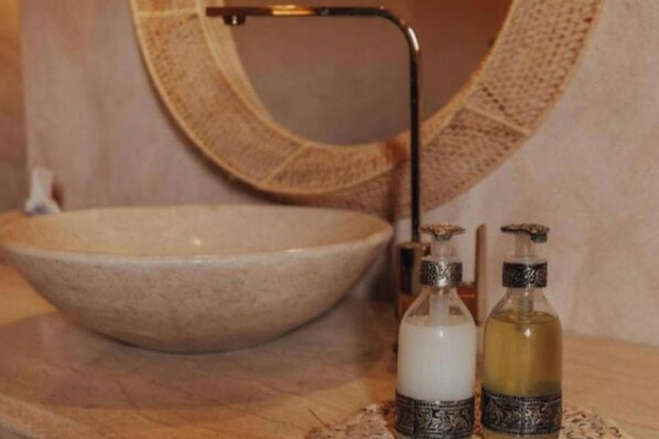 Un lavabo de baño con un recipiente grande, un grifo y dos botellas de jabón líquido.